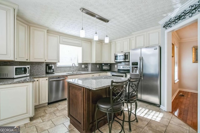 kitchen with sink, a breakfast bar, stainless steel appliances, light stone counters, and a kitchen island