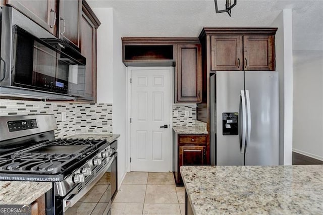 kitchen with tasteful backsplash, dark brown cabinets, light tile patterned floors, stainless steel appliances, and light stone countertops