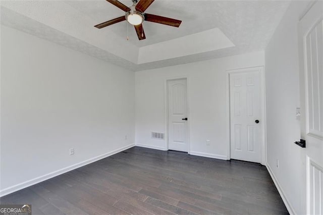 unfurnished bedroom with ceiling fan, dark hardwood / wood-style flooring, and a raised ceiling