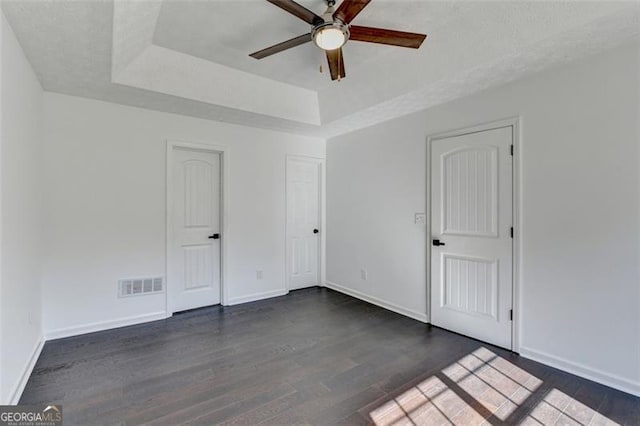 empty room with dark wood-type flooring, ceiling fan, and a raised ceiling