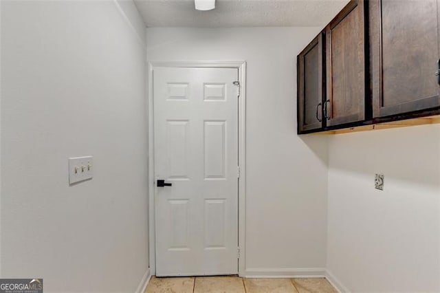 clothes washing area with cabinets, a textured ceiling, and light tile patterned flooring