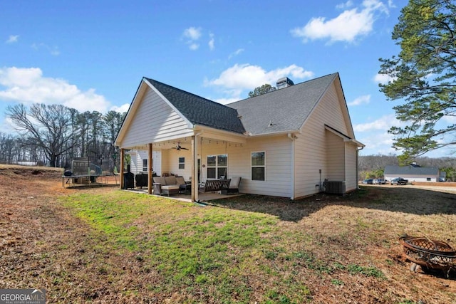 back of property featuring central AC, a patio area, a trampoline, a yard, and an outdoor living space with a fire pit