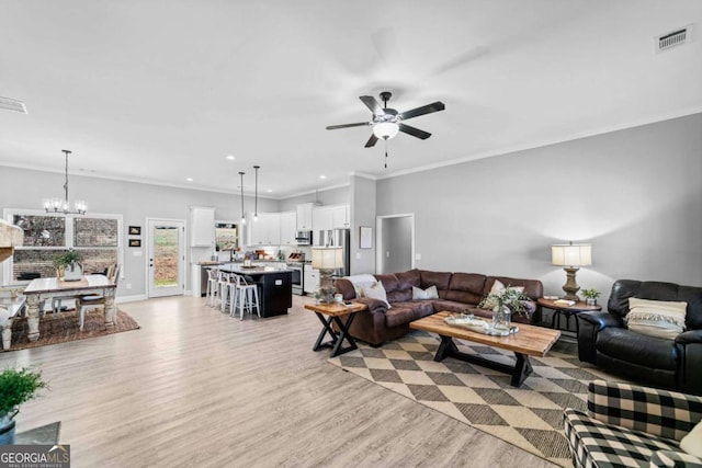 living room with ceiling fan with notable chandelier, ornamental molding, and light hardwood / wood-style floors