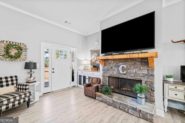 living room with crown molding, a stone fireplace, and light hardwood / wood-style floors