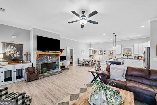 living room featuring ceiling fan with notable chandelier, a fireplace, light hardwood / wood-style floors, and crown molding