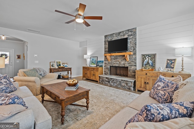 living room with a stone fireplace and ceiling fan