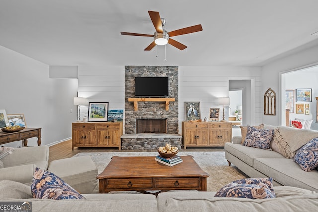 living room with a fireplace, ceiling fan, and light wood-type flooring