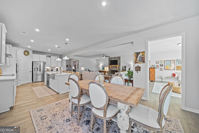 dining room with ceiling fan, a stone fireplace, and light hardwood / wood-style floors