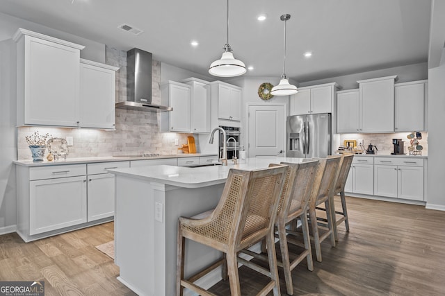 kitchen featuring white cabinetry, a kitchen island with sink, wall chimney exhaust hood, and appliances with stainless steel finishes