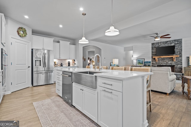 kitchen with decorative light fixtures, an island with sink, white cabinets, a kitchen breakfast bar, and stainless steel appliances