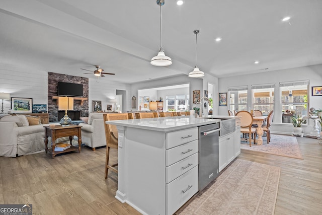 kitchen with light hardwood / wood-style flooring, dishwasher, white cabinetry, a kitchen island with sink, and decorative light fixtures