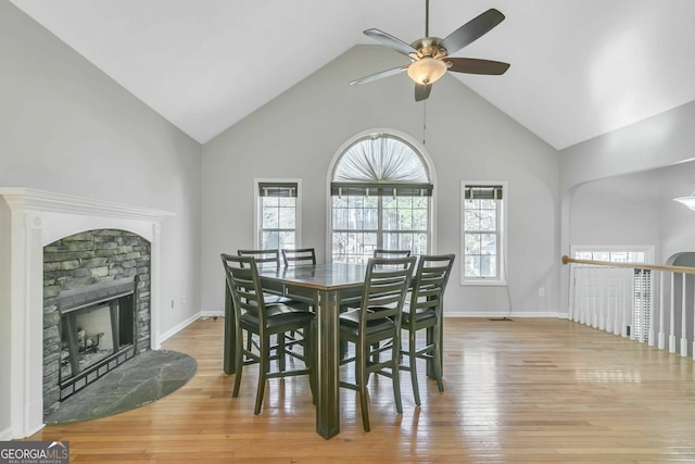 dining space featuring ceiling fan, a stone fireplace, high vaulted ceiling, and light hardwood / wood-style floors