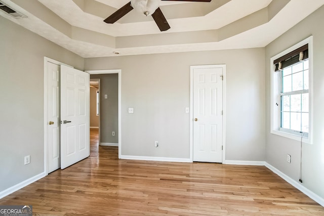 unfurnished bedroom with ceiling fan, a tray ceiling, and light hardwood / wood-style floors