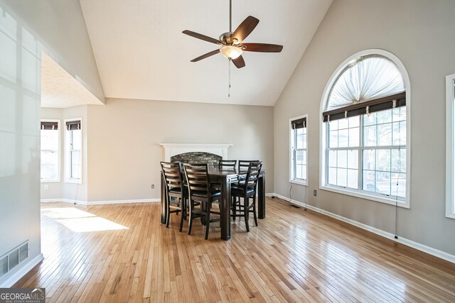 dining space featuring ceiling fan, high vaulted ceiling, a fireplace, and light hardwood / wood-style floors