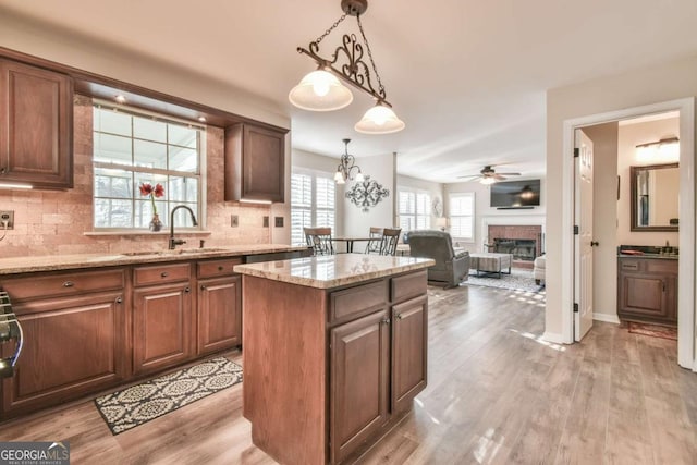 kitchen featuring a kitchen island, pendant lighting, sink, light stone countertops, and light wood-type flooring