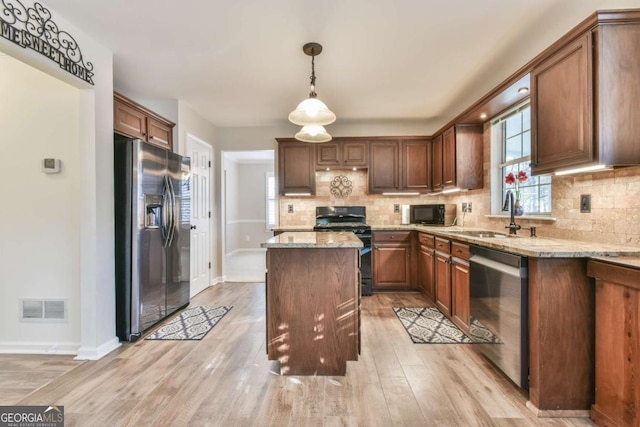 kitchen featuring pendant lighting, sink, light stone counters, and black appliances