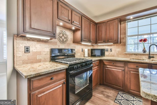 kitchen with sink, black appliances, light hardwood / wood-style flooring, light stone countertops, and backsplash