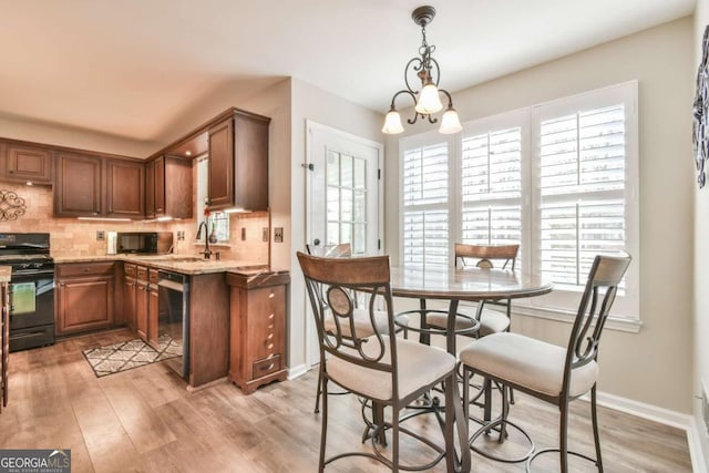 kitchen featuring light stone counters, decorative light fixtures, black appliances, light wood-type flooring, and backsplash