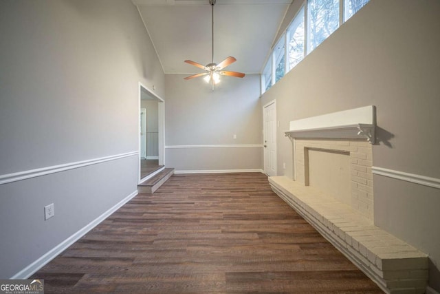 interior space with a brick fireplace, dark hardwood / wood-style floors, ceiling fan, and a towering ceiling