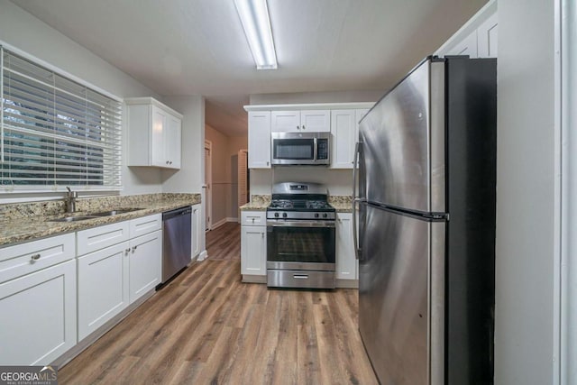 kitchen with sink, appliances with stainless steel finishes, white cabinetry, hardwood / wood-style floors, and light stone countertops