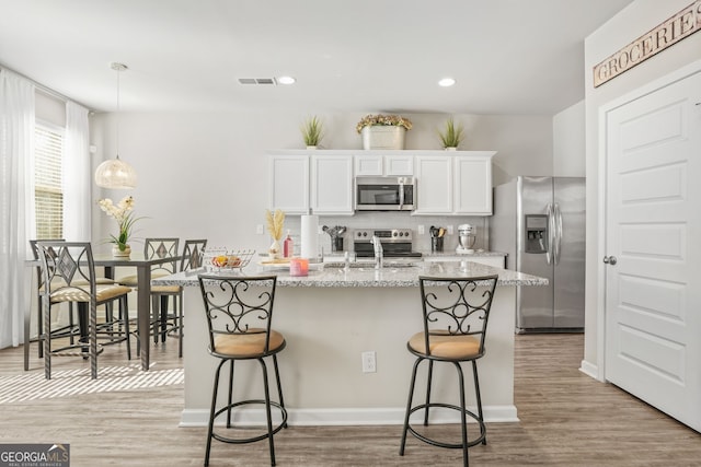 kitchen with sink, a breakfast bar area, stainless steel appliances, light stone countertops, and white cabinets