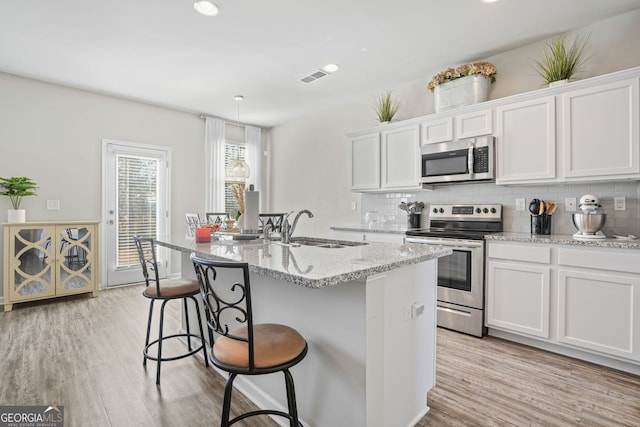 kitchen with white cabinetry, sink, a kitchen island with sink, light stone counters, and stainless steel appliances