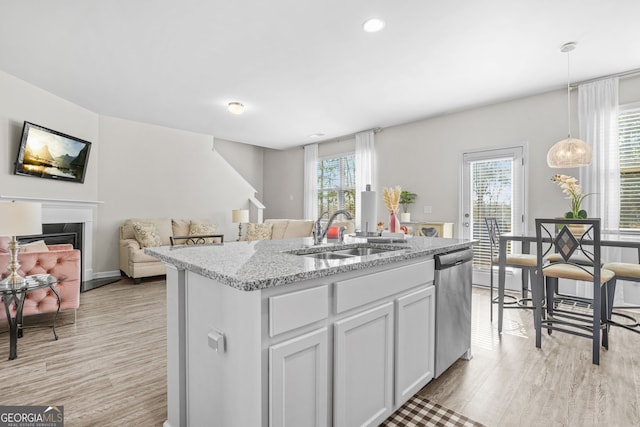 kitchen featuring sink, white cabinetry, decorative light fixtures, stainless steel dishwasher, and an island with sink