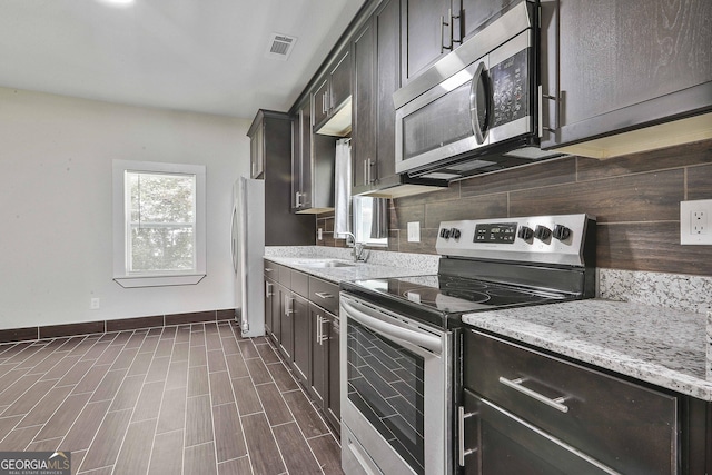 kitchen with sink, tasteful backsplash, light stone counters, dark brown cabinets, and stainless steel appliances