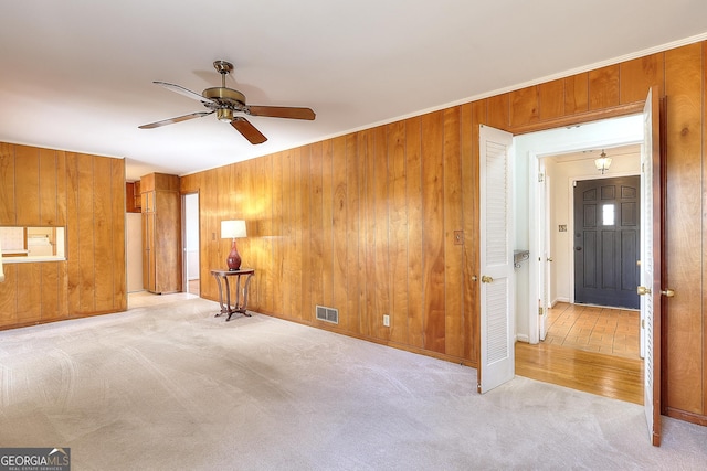 carpeted empty room with crown molding, ceiling fan, and wood walls