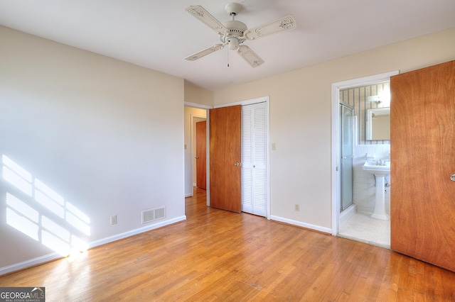 unfurnished bedroom featuring ceiling fan, ensuite bathroom, a closet, and light wood-type flooring