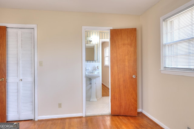 unfurnished bedroom featuring connected bathroom, light wood-type flooring, and a closet