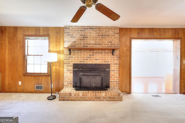 carpeted living room with wooden walls, ceiling fan, and a wood stove