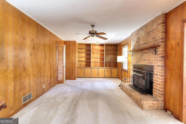 unfurnished living room with built in features, wood walls, ornamental molding, light colored carpet, and ceiling fan