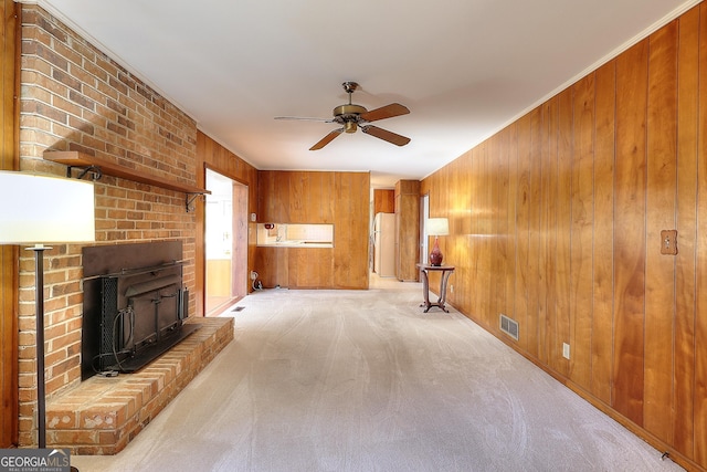 unfurnished living room featuring crown molding, wooden walls, light colored carpet, and ceiling fan