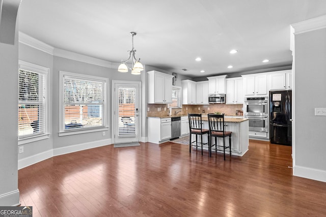 kitchen with a breakfast bar area, stainless steel appliances, hanging light fixtures, white cabinetry, and a kitchen island