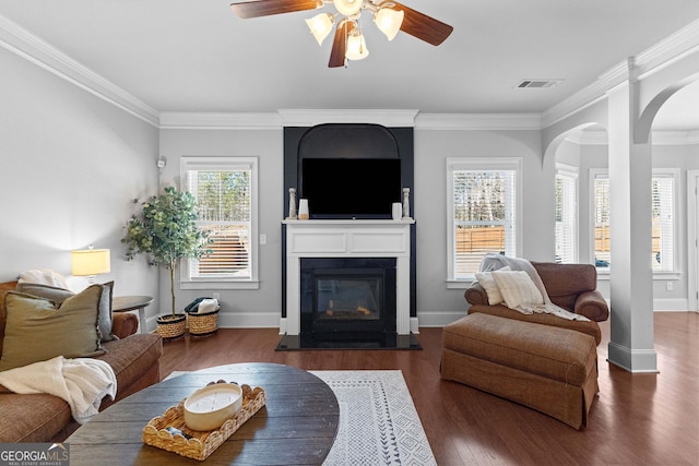 living area with crown molding, visible vents, dark wood-type flooring, a glass covered fireplace, and baseboards