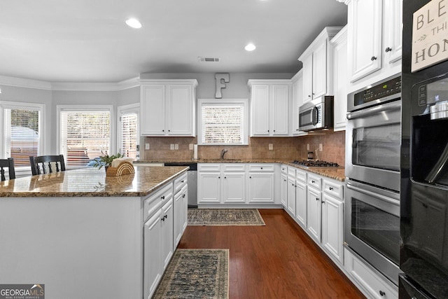 kitchen with visible vents, appliances with stainless steel finishes, white cabinets, a sink, and dark stone countertops