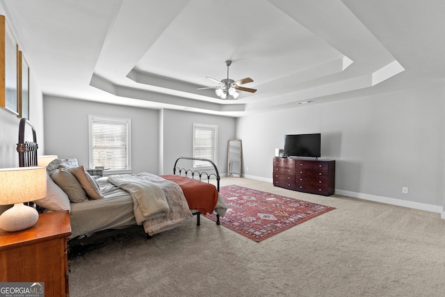 bedroom with a raised ceiling, light colored carpet, ceiling fan, and baseboards