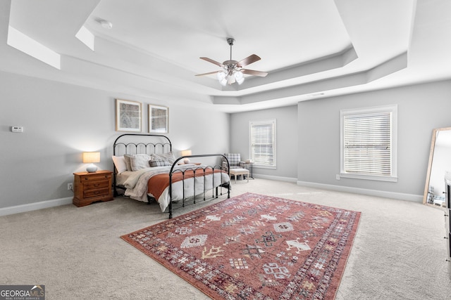 bedroom featuring a raised ceiling, light carpet, and baseboards