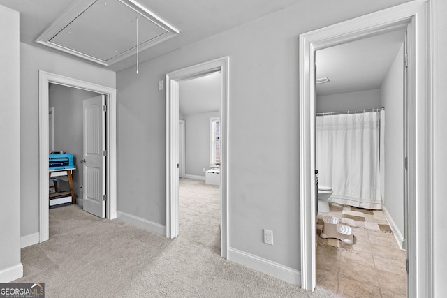 hall featuring light colored carpet, attic access, and baseboards