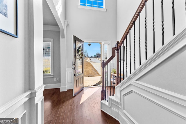 foyer with a wealth of natural light, dark wood finished floors, a decorative wall, and stairs