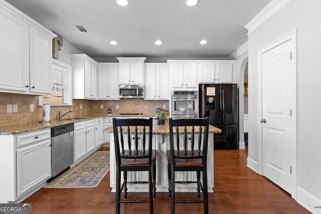 kitchen with white cabinets, stone countertops, a kitchen island, and stainless steel appliances