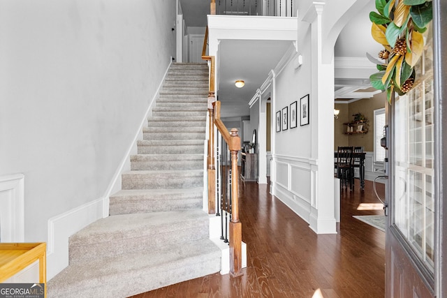 stairway featuring a wainscoted wall, crown molding, a decorative wall, and wood finished floors