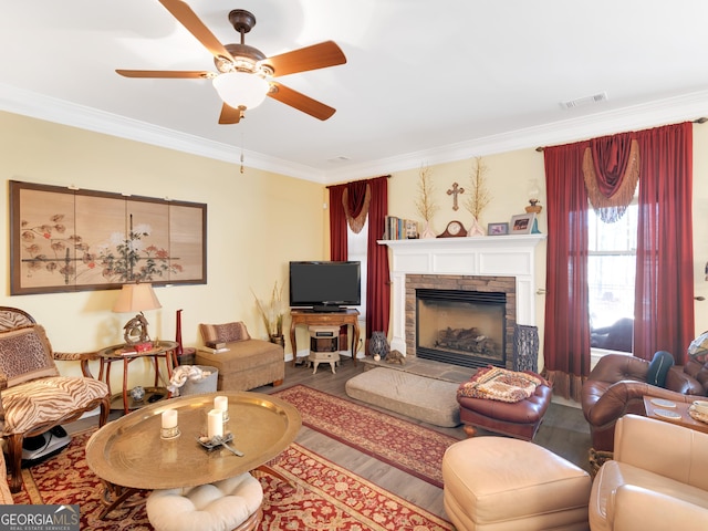 living room featuring crown molding, wood-type flooring, a stone fireplace, and ceiling fan