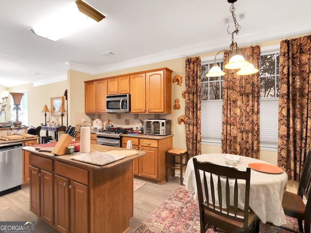 kitchen with stainless steel appliances, ornamental molding, light hardwood / wood-style floors, a kitchen island, and decorative light fixtures