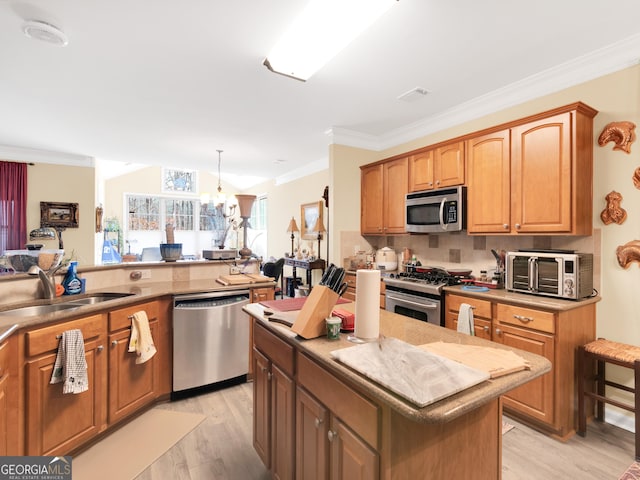 kitchen featuring sink, hanging light fixtures, stainless steel appliances, a center island, and ornamental molding