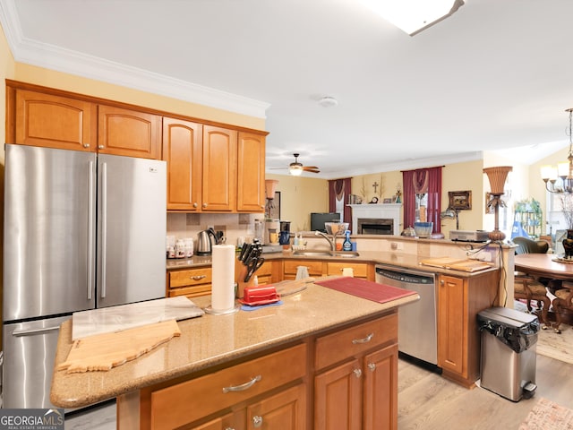 kitchen with sink, appliances with stainless steel finishes, ceiling fan with notable chandelier, kitchen peninsula, and light wood-type flooring