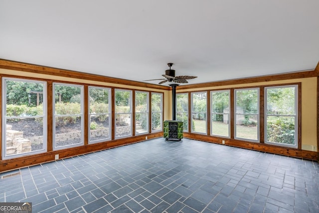 unfurnished sunroom with plenty of natural light, a wood stove, and ceiling fan