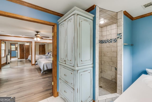 bathroom with crown molding, wood-type flooring, a tile shower, vanity, and ceiling fan