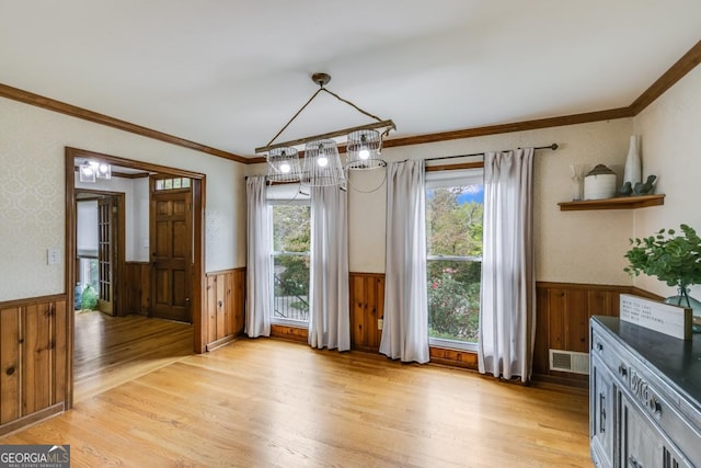 unfurnished dining area featuring ornamental molding, wood walls, and light wood-type flooring